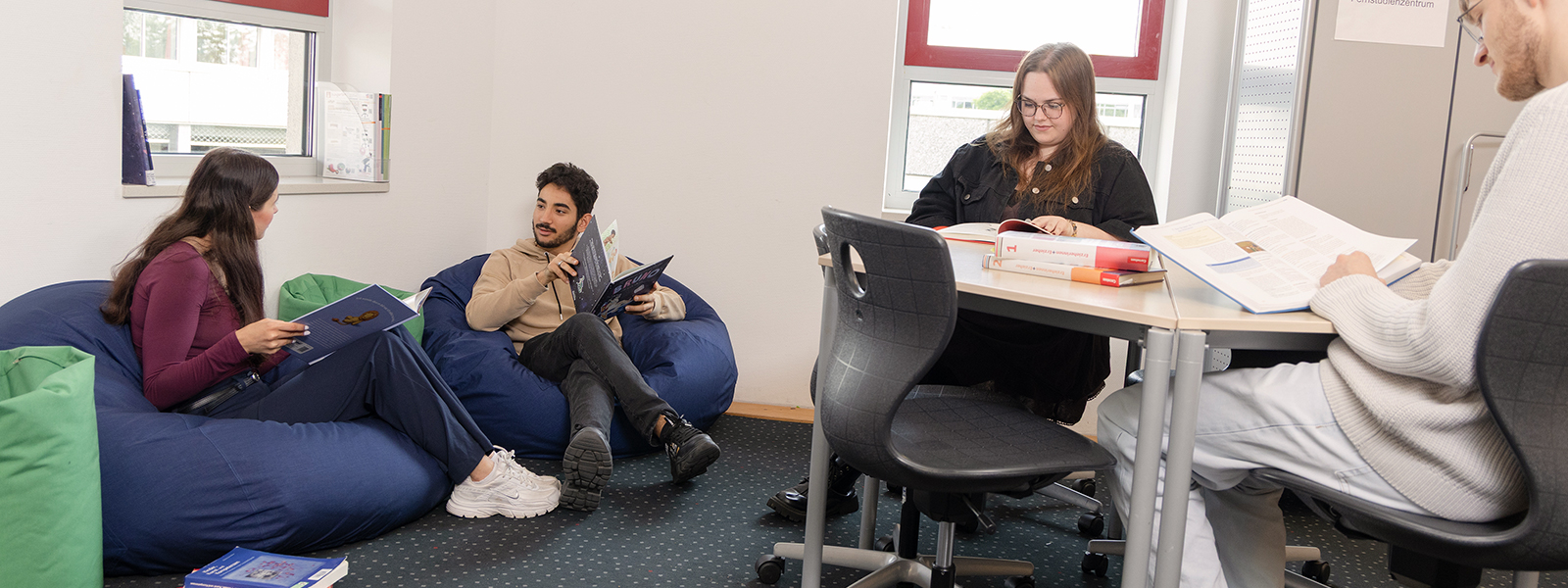 SChüler/-innen sitzen und lesen und unterhalten sich in der Schulmediathek