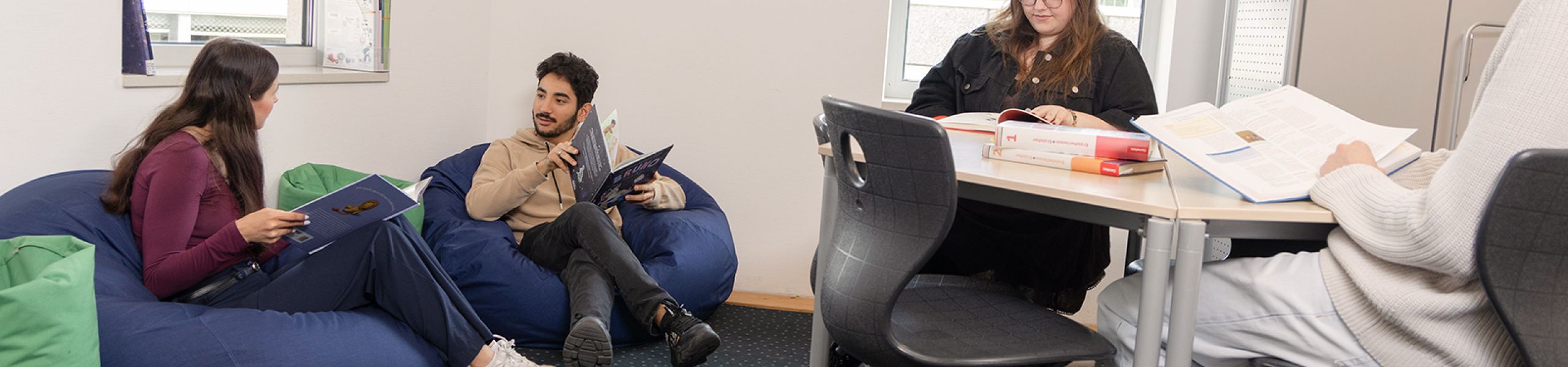 SChüler/-innen sitzen und lesen und unterhalten sich in der Schulmediathek